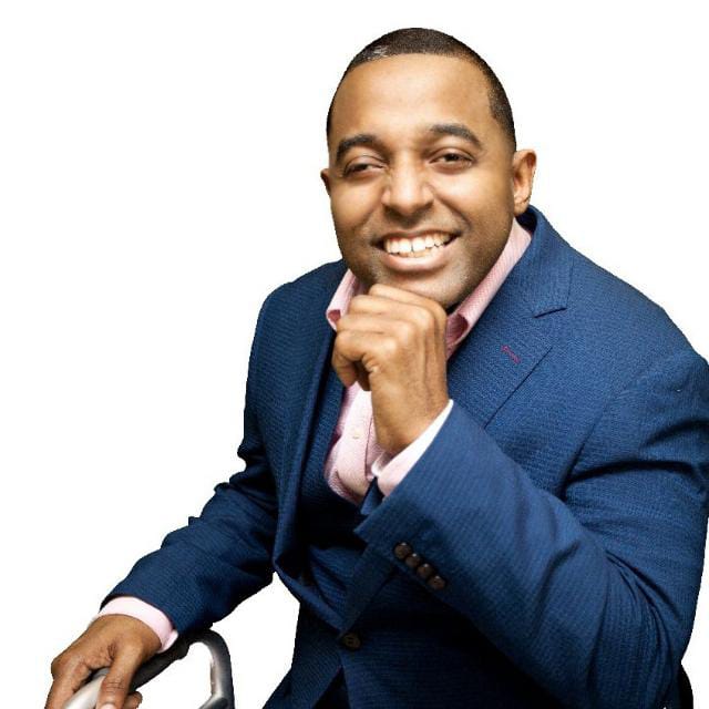 Pastor Richie Ramos sentado, sonriendo y vestido con traje azul